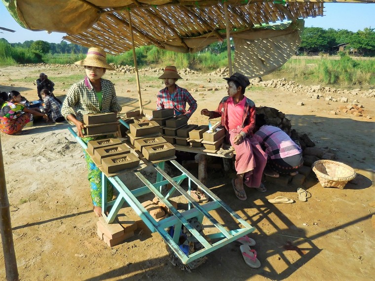 Eine Burmesin fährt mit einer Schubkarre die Lehmsteine zum Trocknen